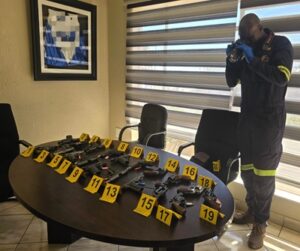 Rows of seized firearms displayed on a table with police evidence markers.