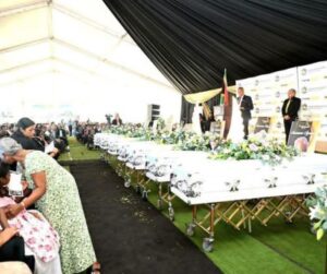 Thamsanqa Ntuli speaking in front of coffins at Monswamy family funeral